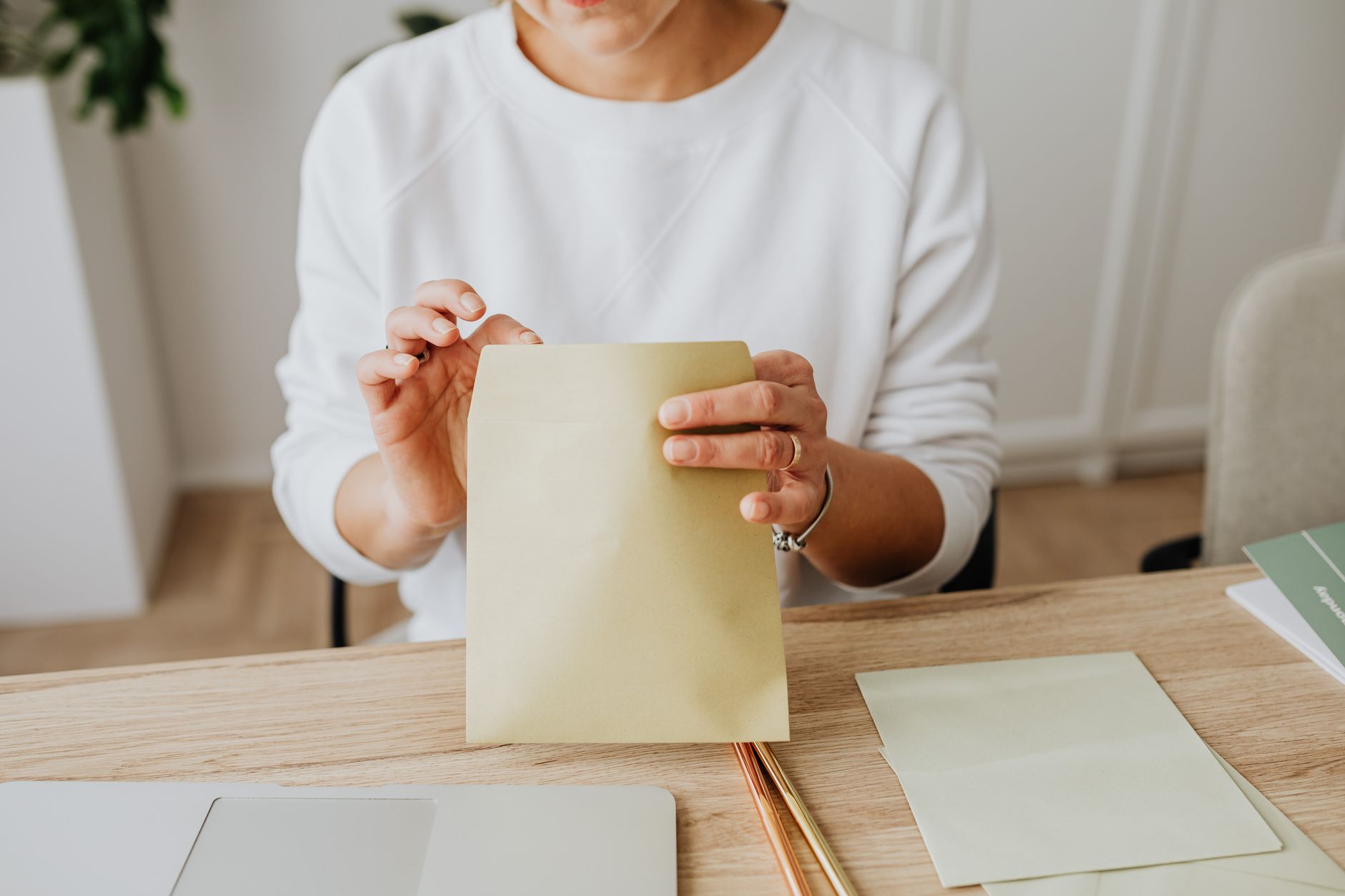 Mujer cerrando un sobre de papel en su escritorio, junto a su laptop, antes de llevarlo al correo