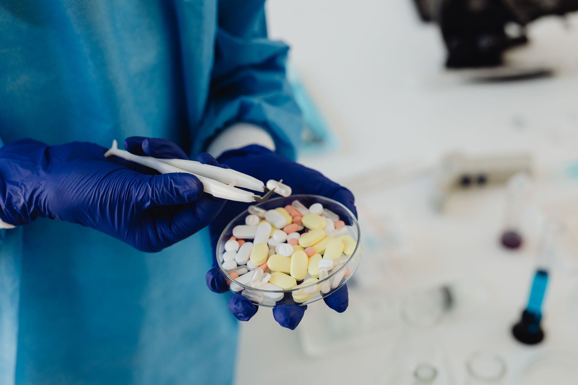 Manos enguantadas sostienen una placa de Petri llena de pastillas en un laboratorio farmacéutico