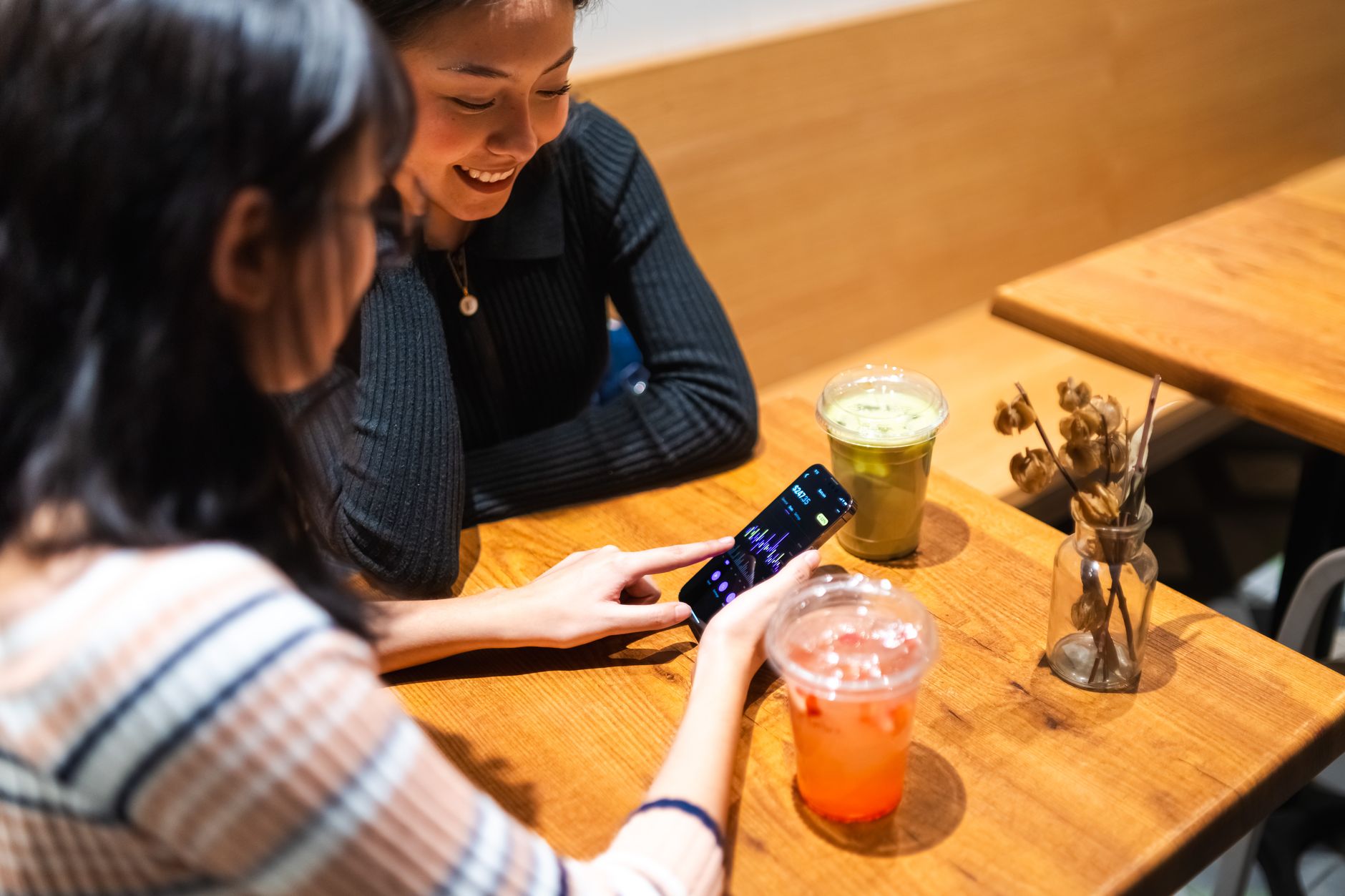 Dos amigas sentadas en una cafetería revisan juntas el gráfico de una aplicación de inversión en el teléfono