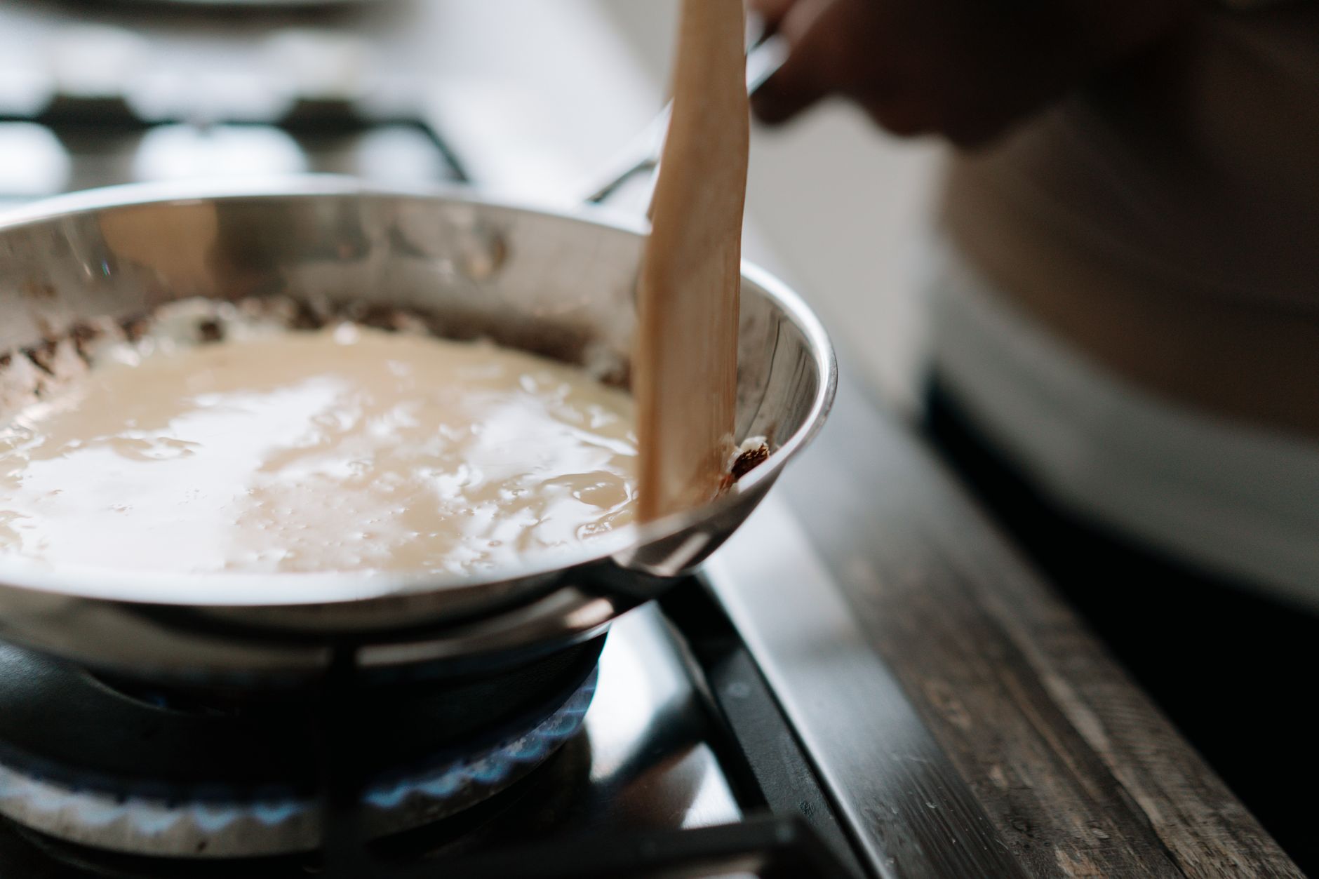 Salsa blanca de leche espesando en una sarten al fuego mientras se remueve con una espatula de madera