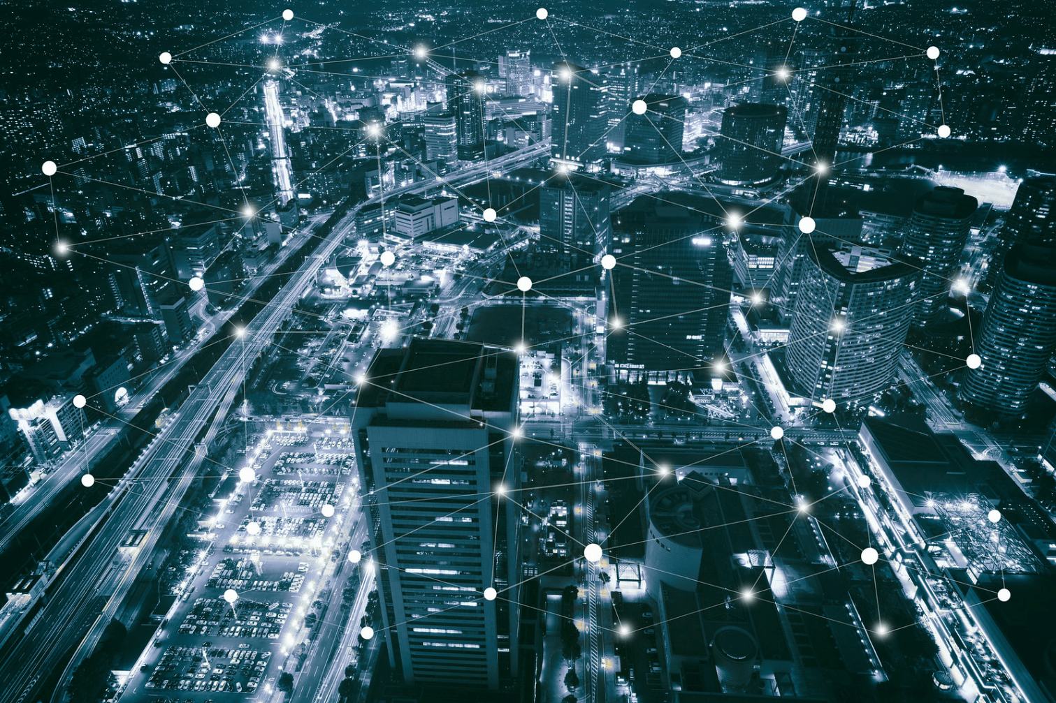 Vista aérea nocturna de una ciudad iluminada con rascacielos y calles, superpuesta con una red de puntos conectados