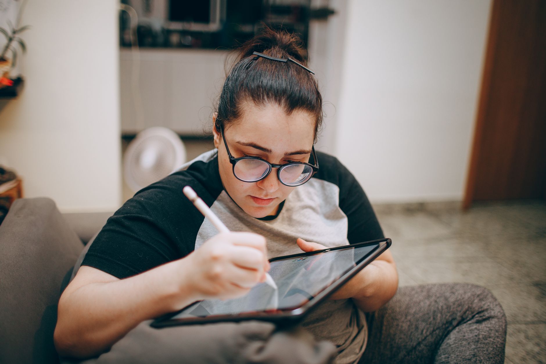 Mujer joven dibuja arte digital con un lápiz óptico sobre una tableta sentada en el sofá de su casa