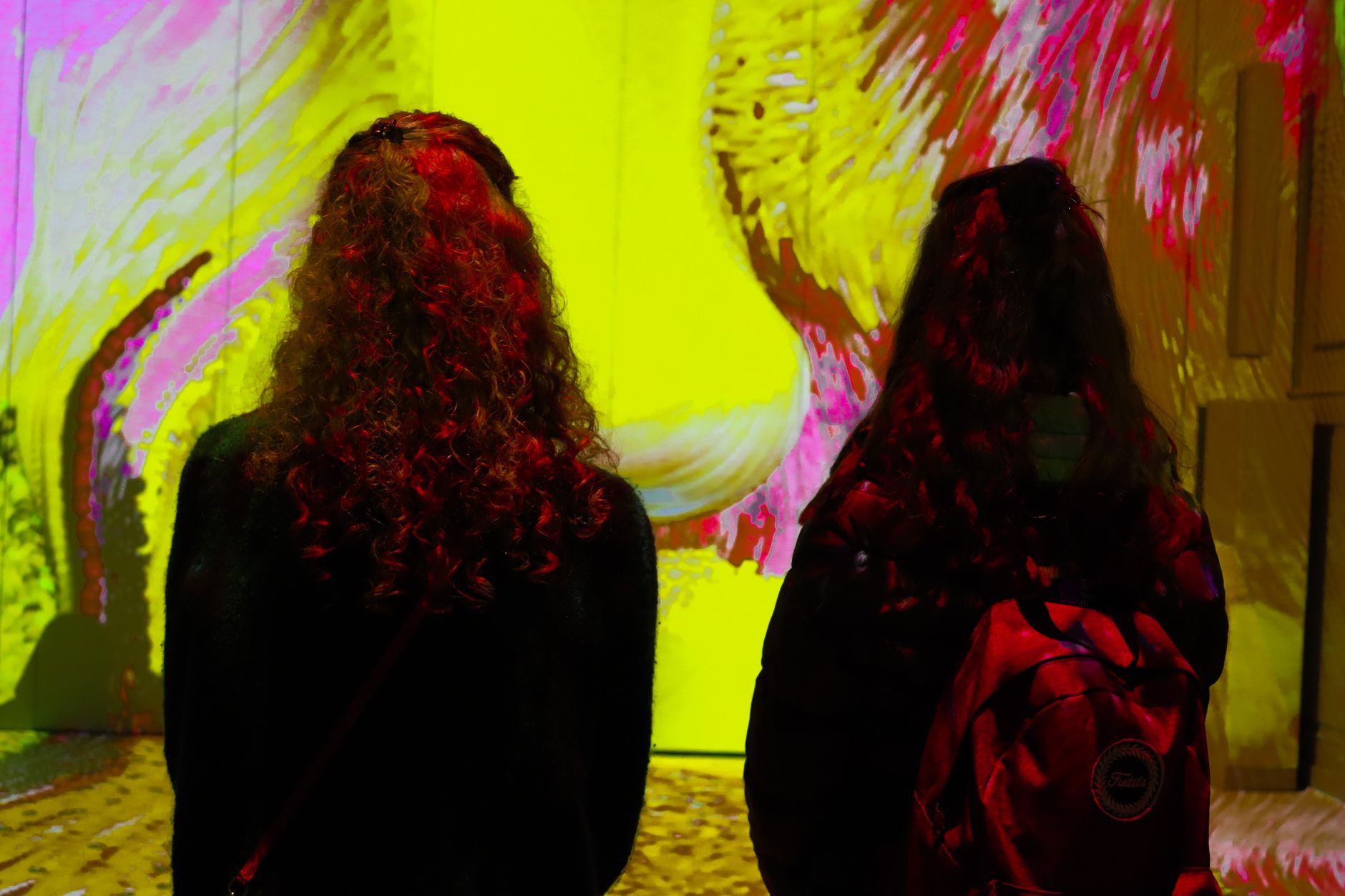 Dos visitantes de espaldas frente a una gran proyección de arte digital en una sala de exposición