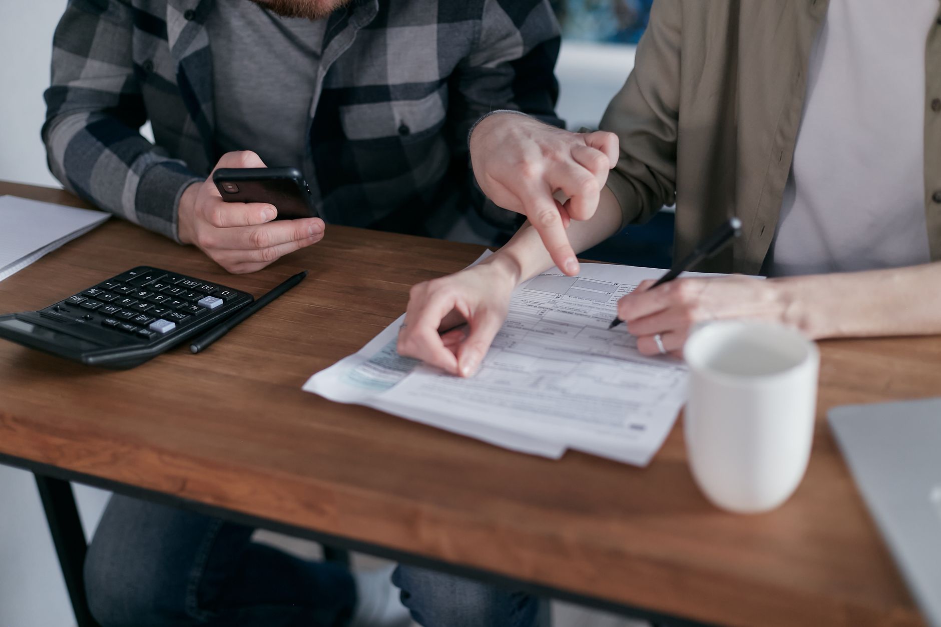 Dos personas hacen cuentas con una calculadora y documentos financieros sobre una mesa de madera