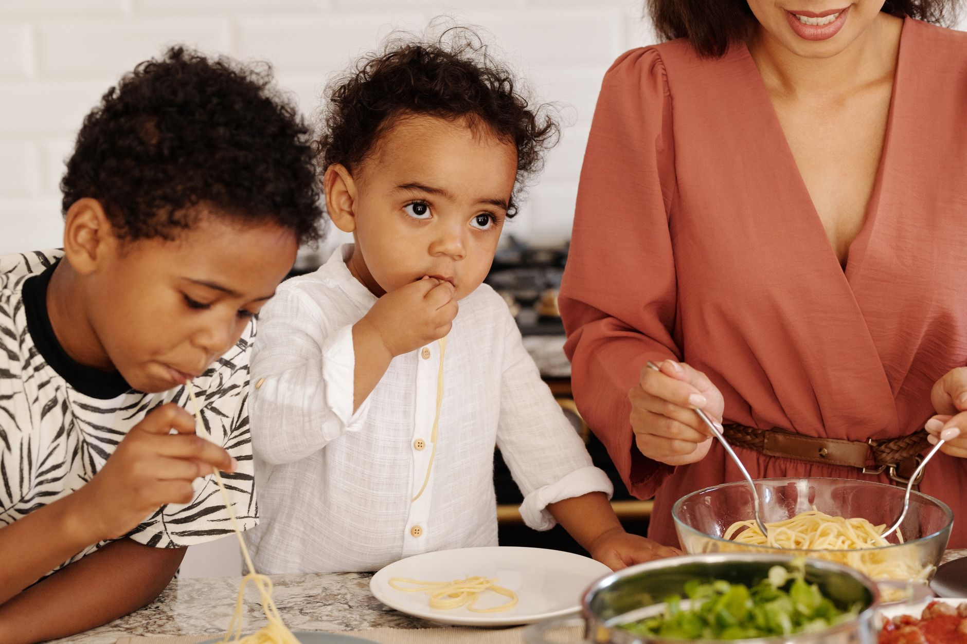 Una madre sirve pasta a sus dos hijos pequenos en la cocina de casa