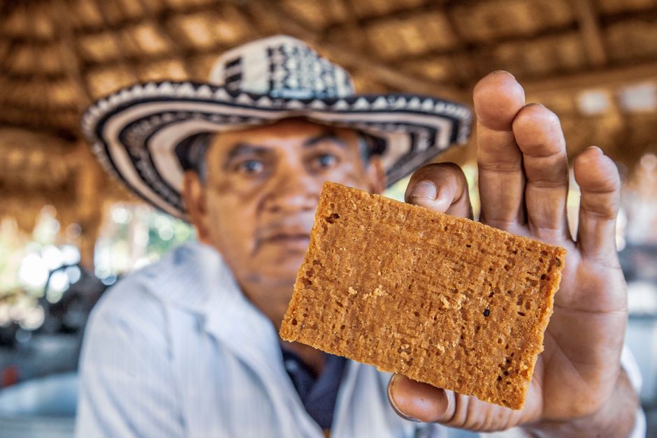 Un hombre con sombrero de rayas muestra una tableta rectangular de panela de color caramelo