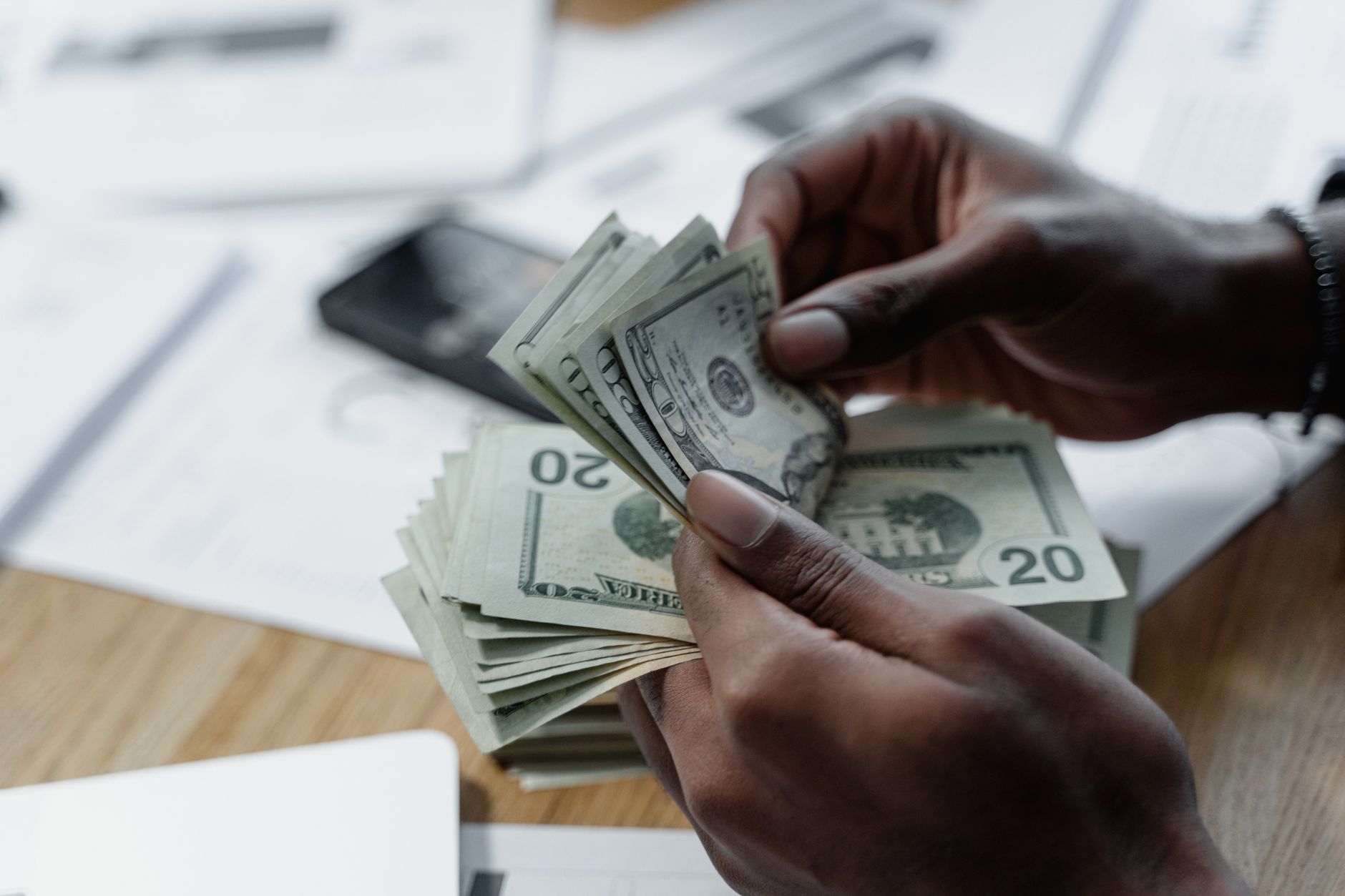 Manos contando billetes de veinte dólares sobre una mesa cubierta de formularios y papeles