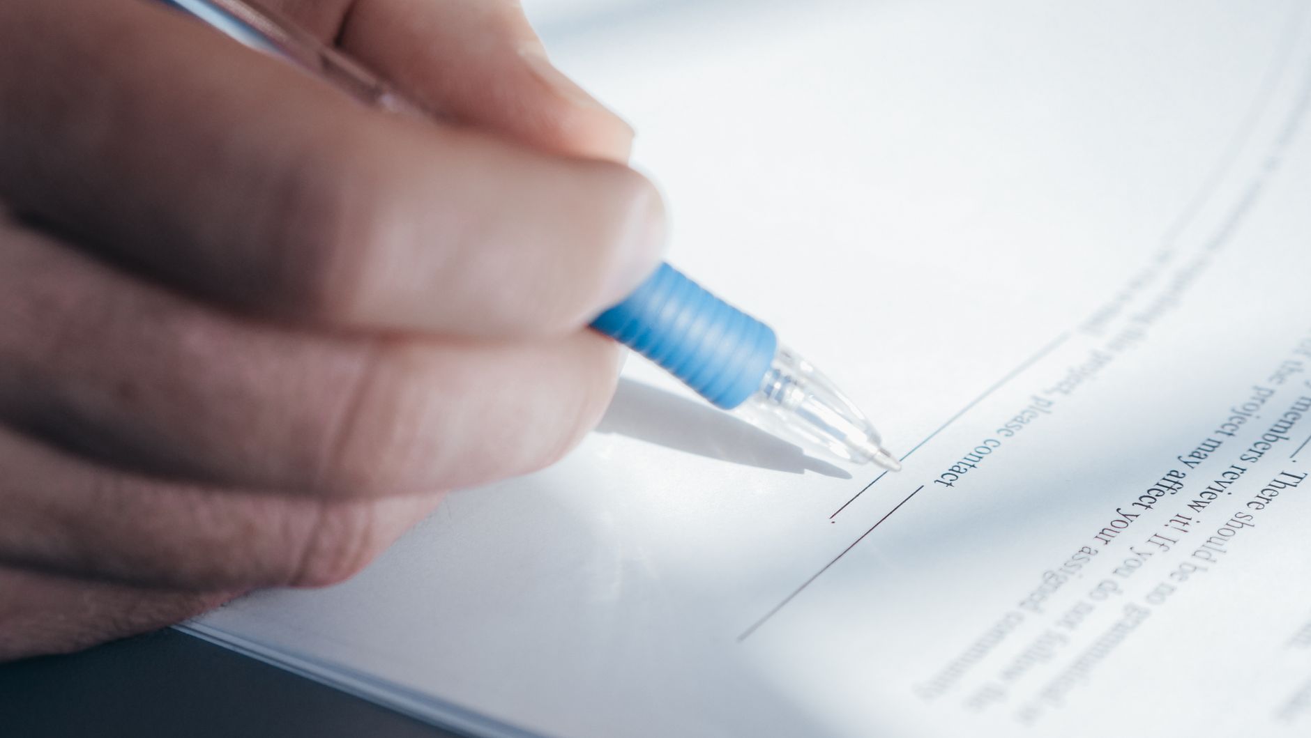 Mano con un bolígrafo azul apoyada sobre la línea de firma de un documento impreso