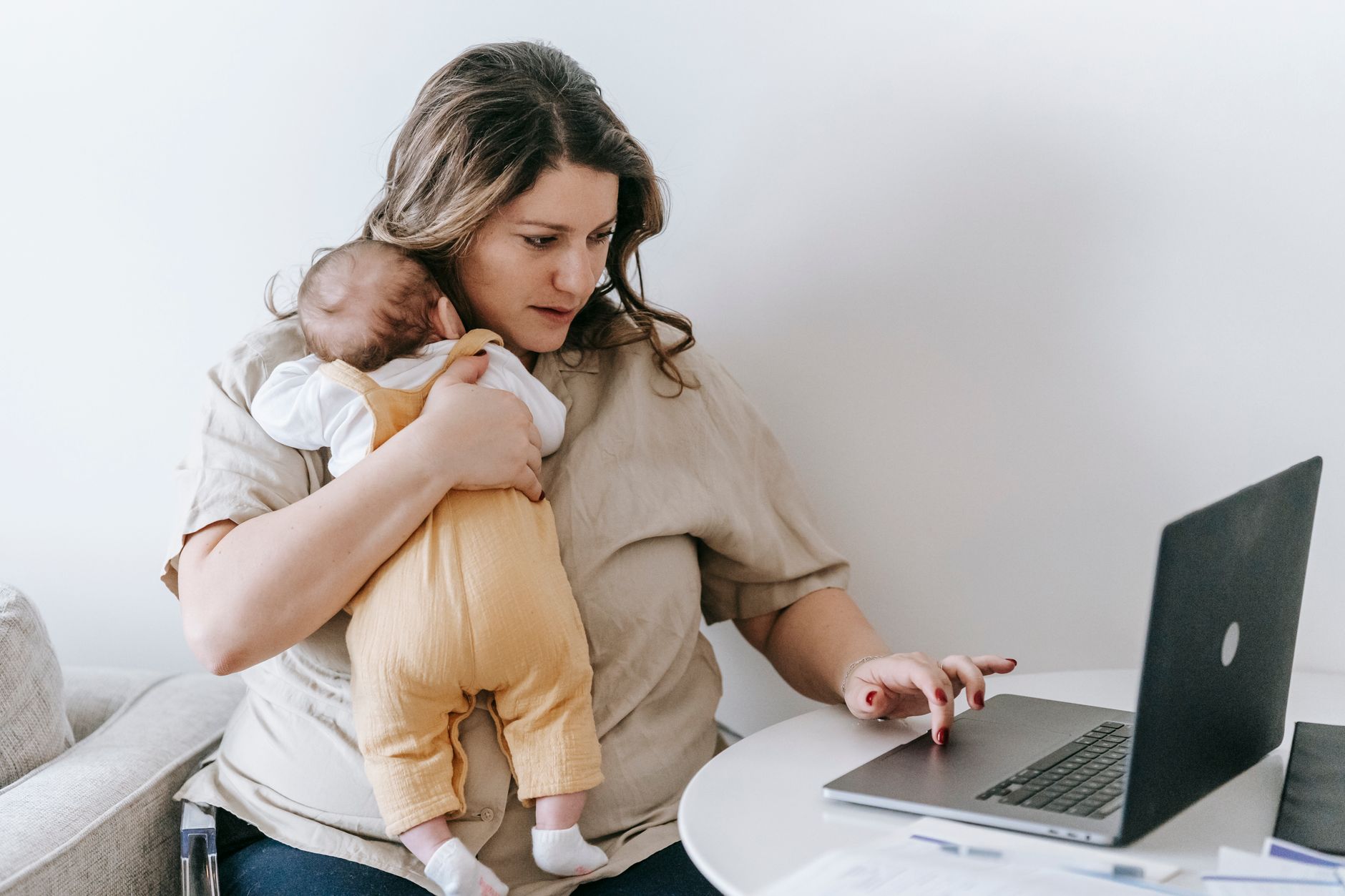 Una madre con su bebé recién nacido en brazos completa un cuestionario en su laptop desde el sofá de casa