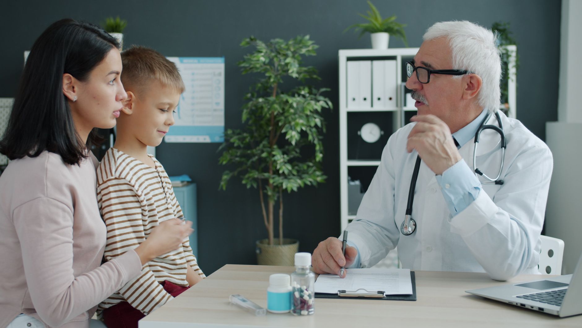 Una madre escucha al médico con su hijo pequeño sentado en el regazo durante una consulta pediátrica