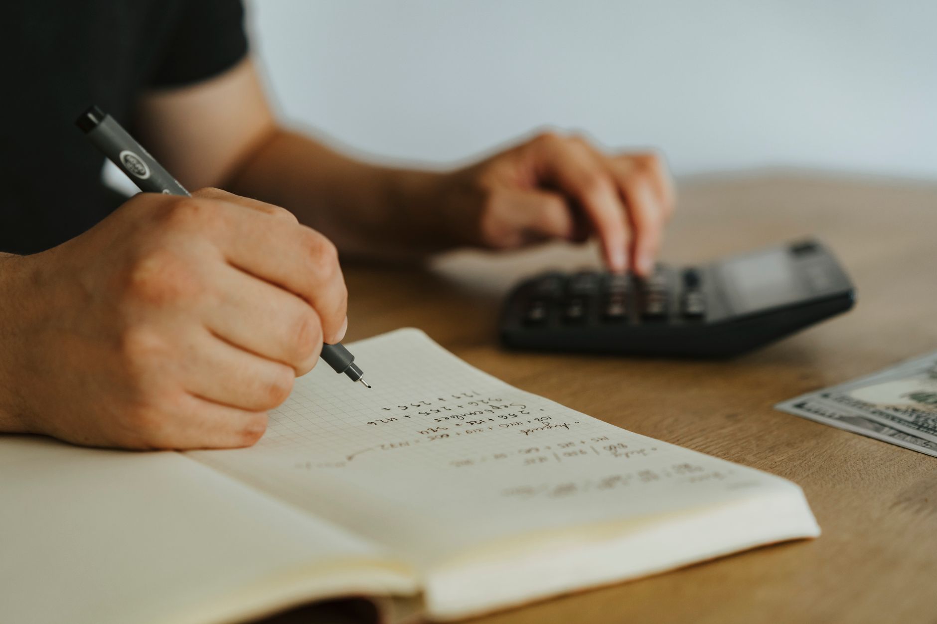 Manos anotando cuentas en una libreta cuadriculada junto a una calculadora sobre una mesa de madera