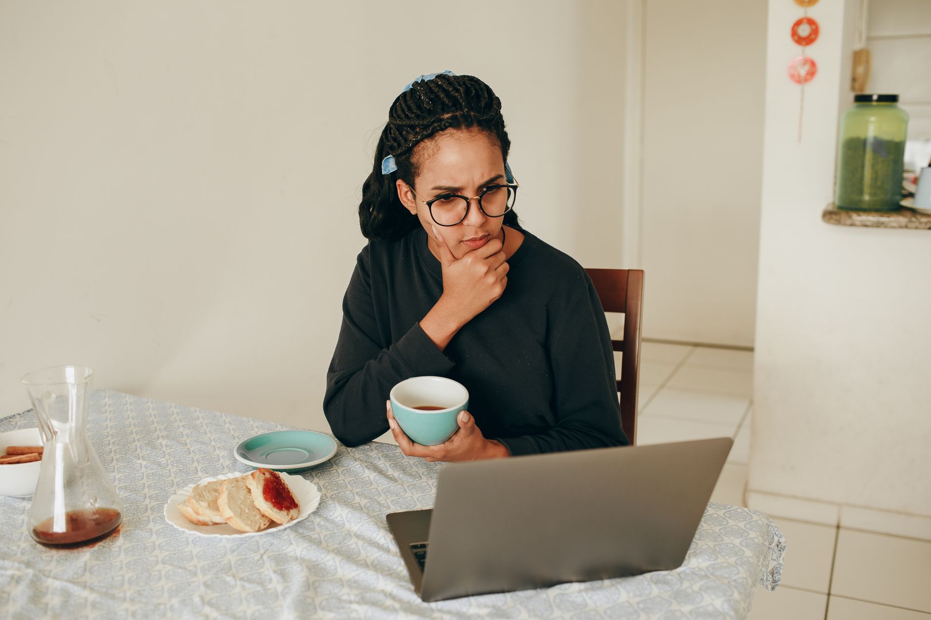 Mujer compara con calma las opciones en la laptop mientras desayuna en la mesa de la cocina