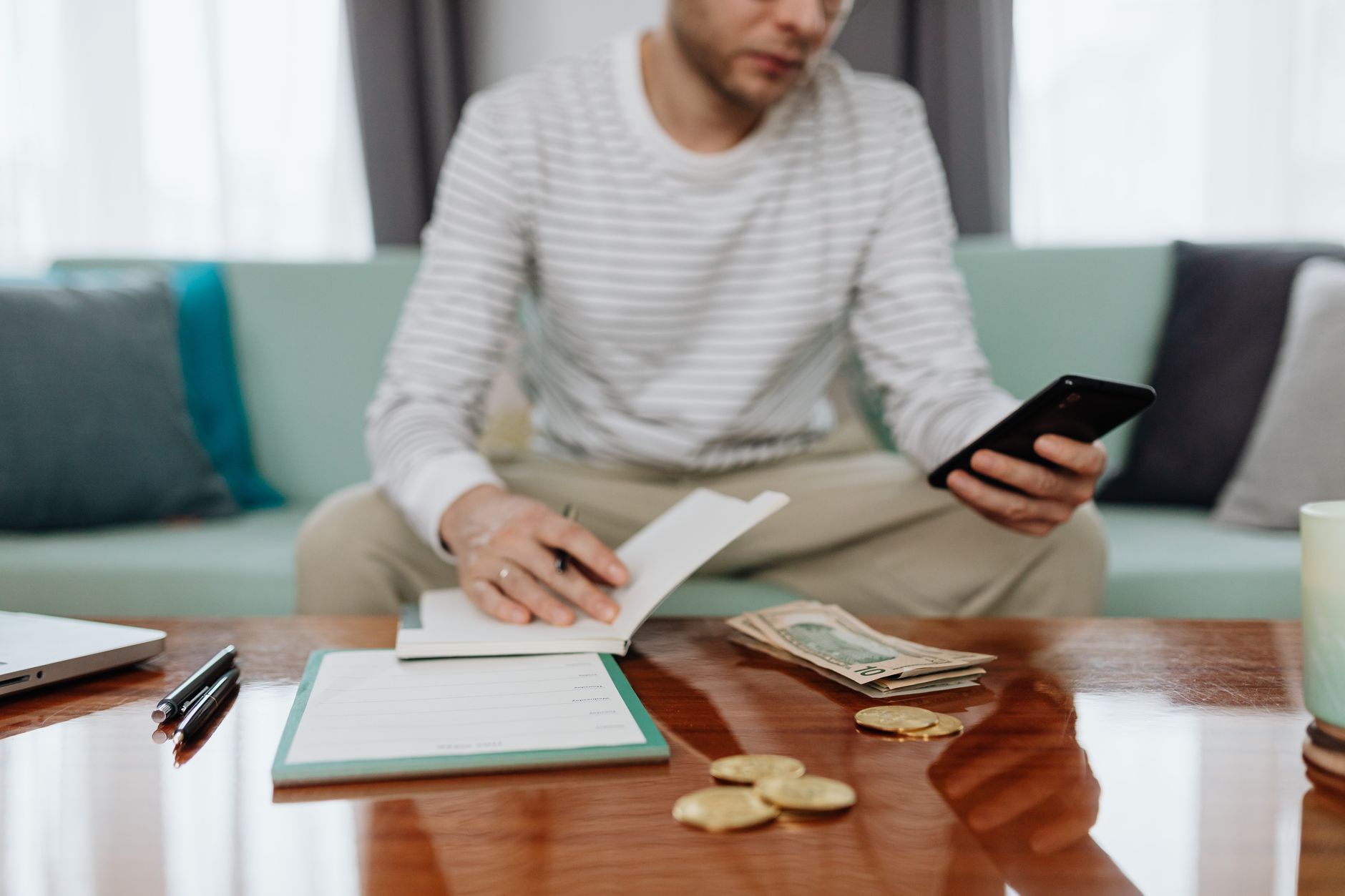 Hombre aparta el dinero del deposito en la mesa de la sala con el celular en la mano