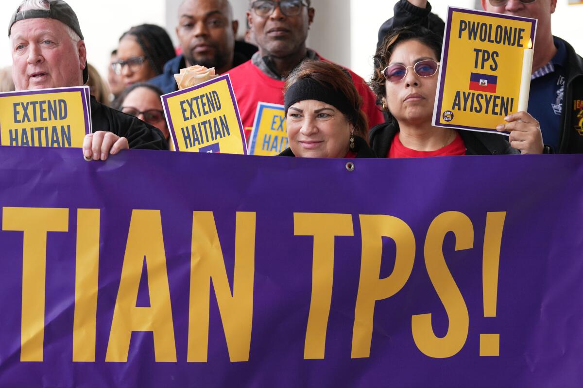 Manifestantes sosteniendo una pancarta morada que dice TIAN TPS y carteles amarillos con los textos EXTEND HAITIAN y PWOLONJE TPS AYISYEN