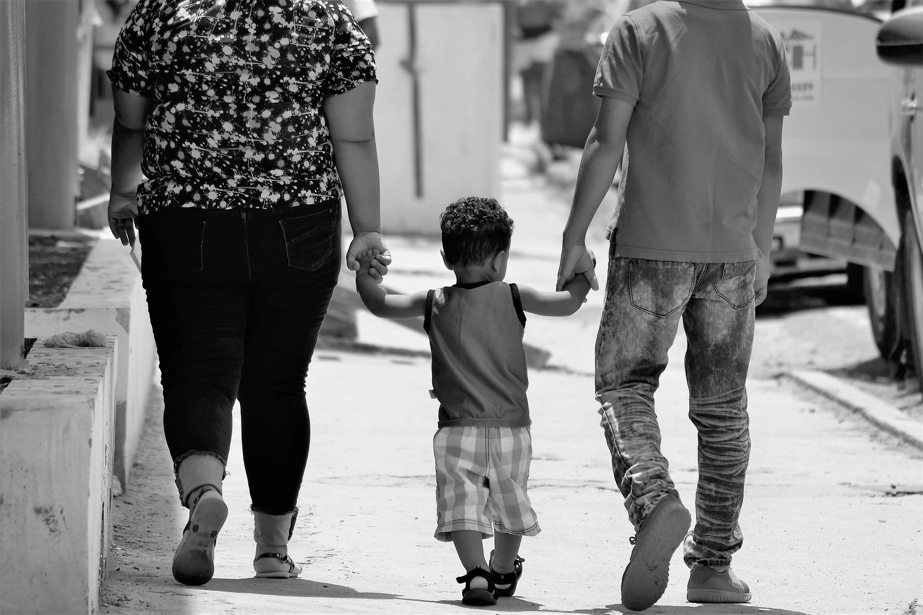 Una madre y un padre caminan de la mano con su hijo pequeño por una calle soleada