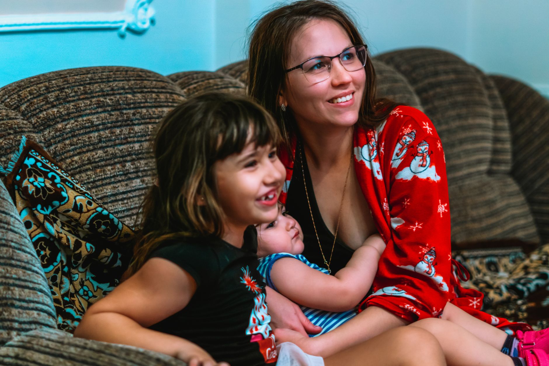 Una madre abraza a sus dos hijas pequeñas sentadas en el sofá de la casa