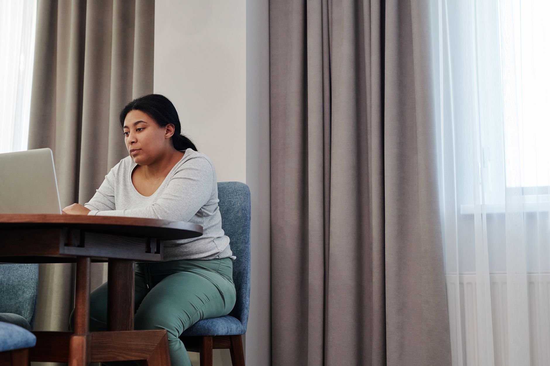 Una mujer consulta información en el portátil sentada a la mesa del comedor de su casa