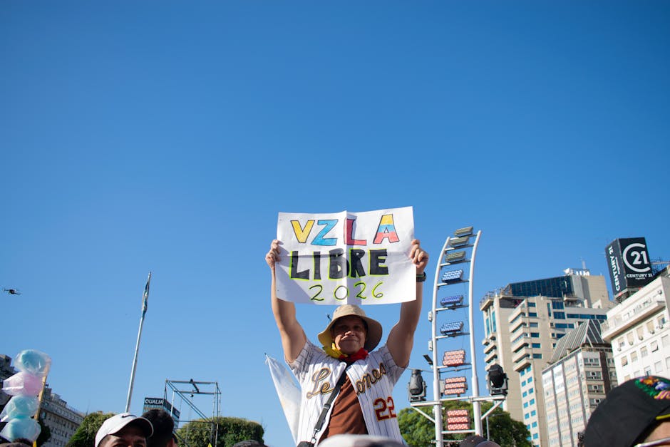 Hombre con sombrero sosteniendo un cartel blanco que dice VZLA LIBRE 2026 en medio de una manifestación